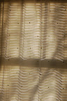 Morning sun peeping through the blinds makes wavy lines on the curtains. 